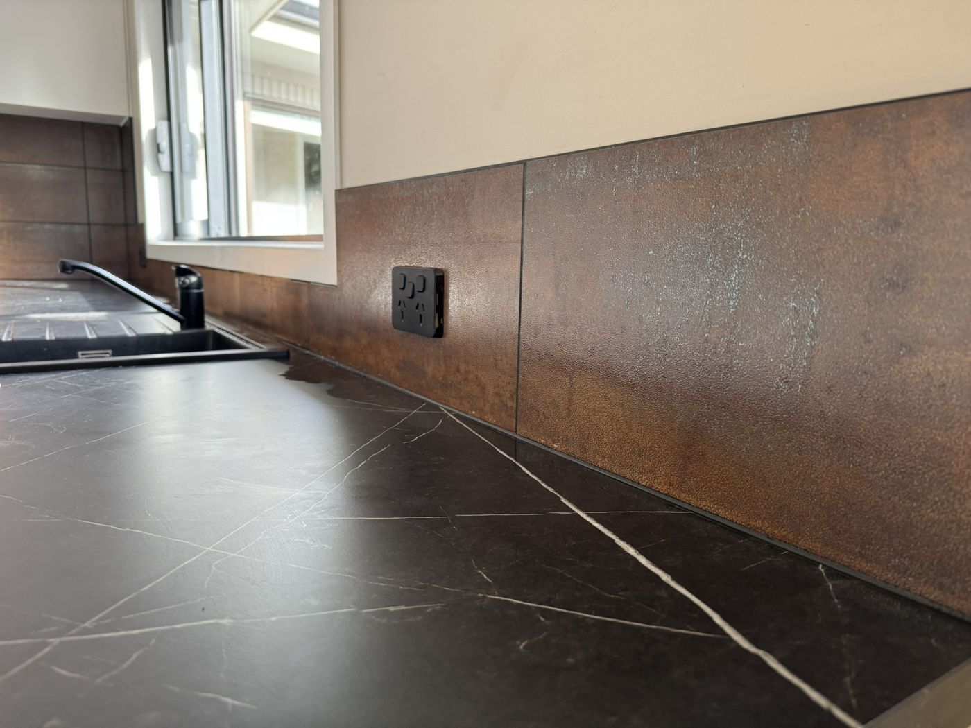 Modern tiled splashback in a new kitchen with a black power point
