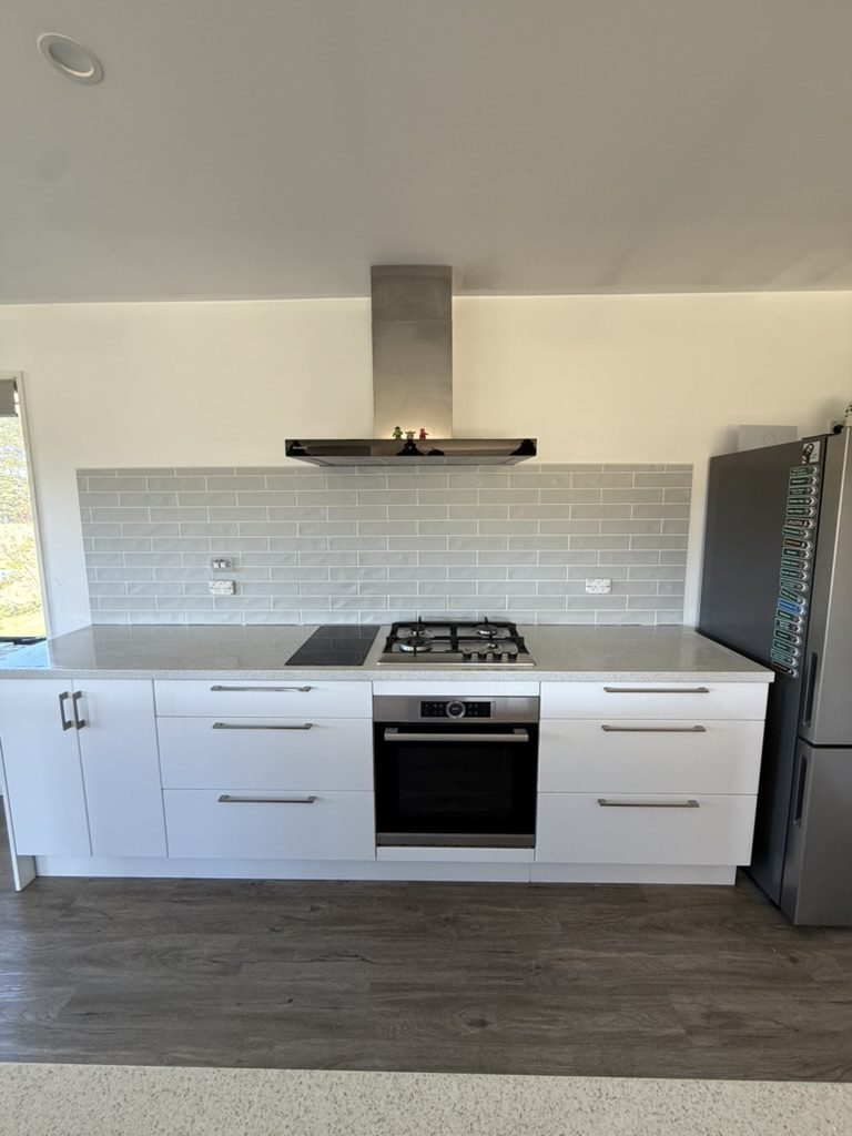 New kitchen with a grey subway tile splashback behind the cooktop and rangehood