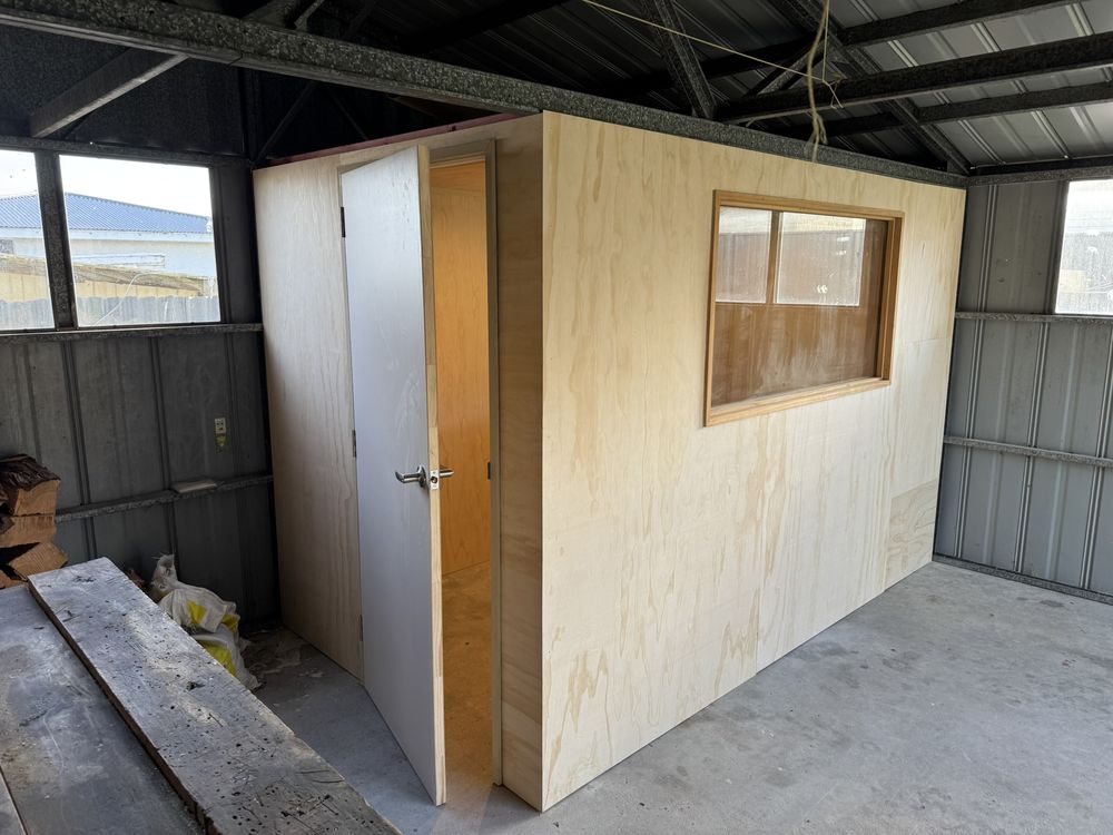Plywood room with door and window built inside a garage